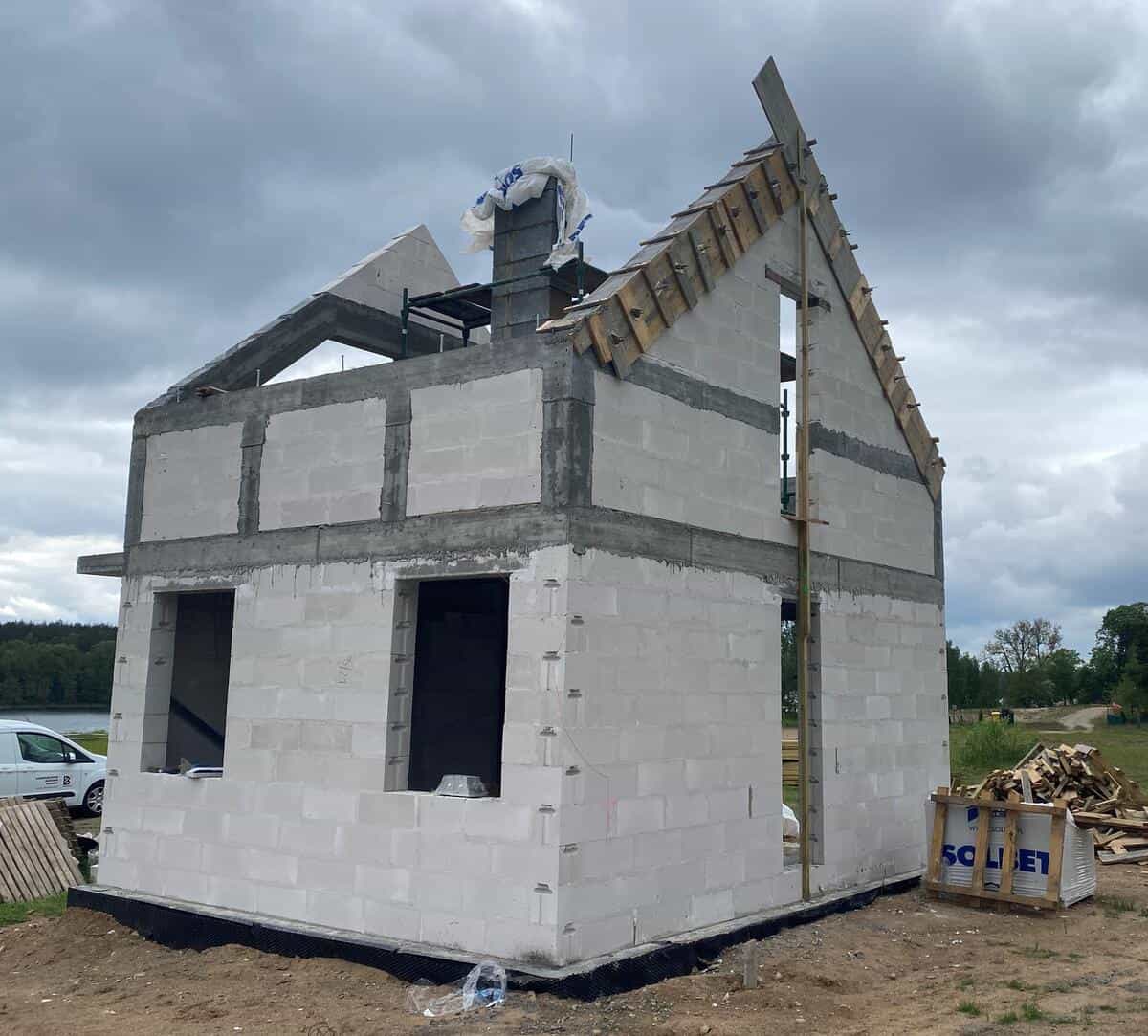 Stan surowy budynku w Dołgiem — murowane ściany i konstrukcja dachu z widokiem na jezioro