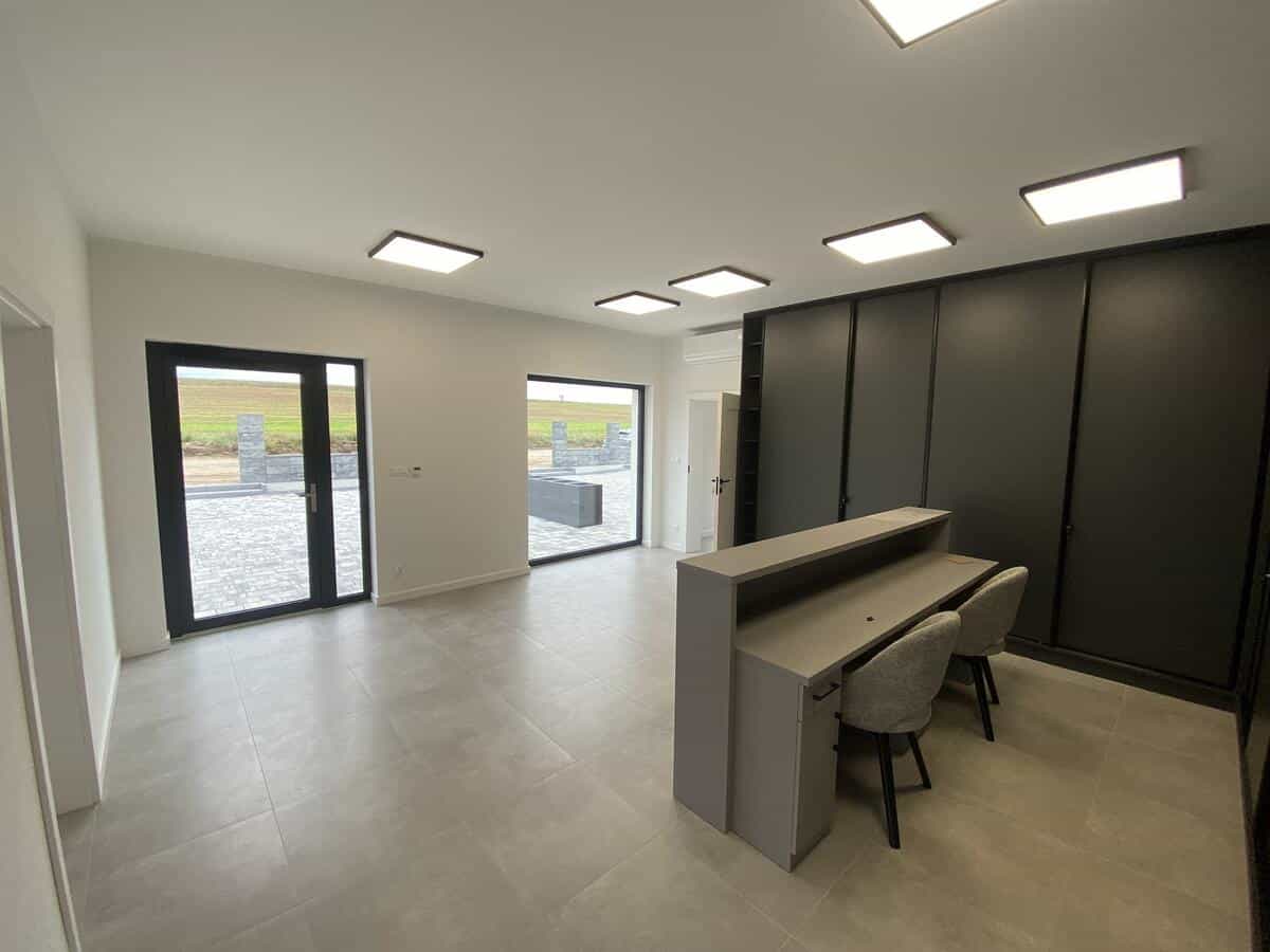 Wnętrze biura domowego z ciemną zabudową meblowa i przeszklonymi drzwiami tarasowymi