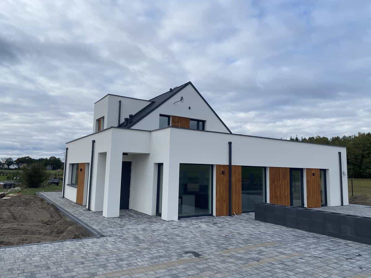 Frontowa elewacja domu z drewnianymi okiennicami i białymi ścianami