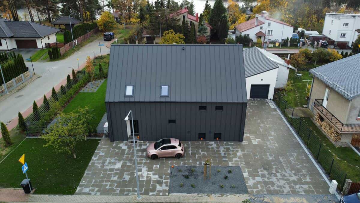 Widok z drona na ukończony budynek z ciemną elewacją z blachy na rąbek i kostką brukową